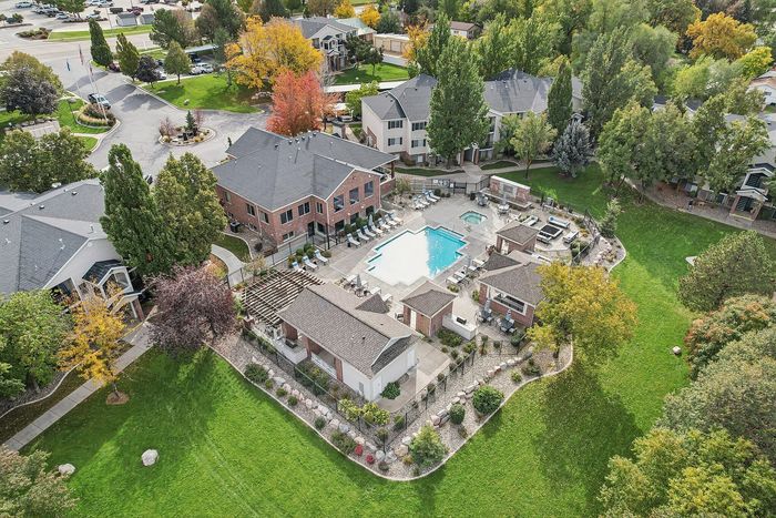 Stunning aerial view of a vibrant apartment complex with a central pool, lush greenery, and cozy seating areas surrounded by trees in a serene neighborhood.