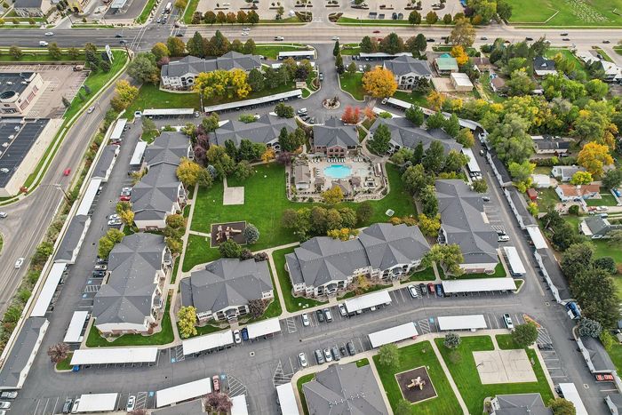 Aerial view of a vibrant apartment complex with landscaped gardens, central pool area, and ample parking, showcasing a serene and inviting community atmosphere.