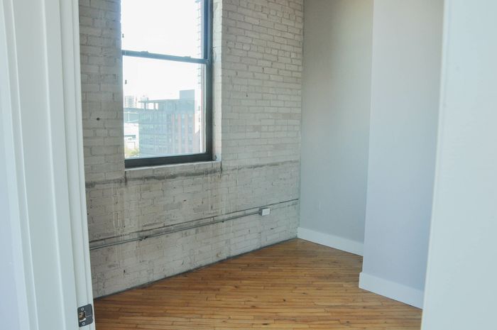 Bright loft space featuring exposed brick, large window with city views, and elegant wood flooring.