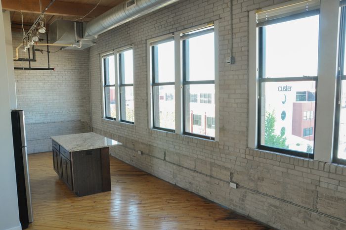 Bright modern loft with exposed brick, large windows, and a sleek kitchen island, perfect for urban living.
