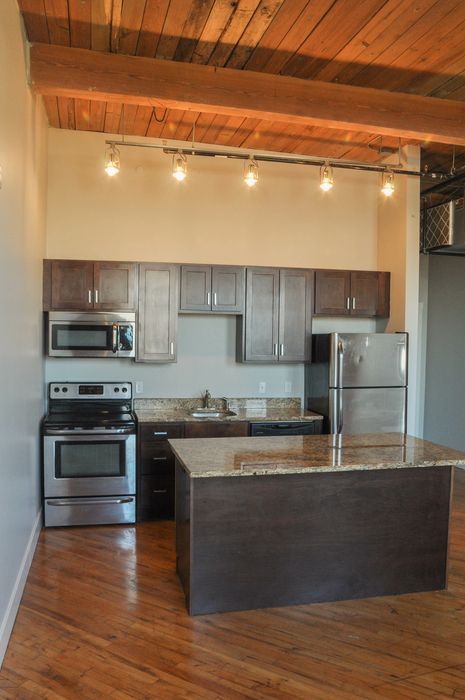 Chic kitchen featuring dark wood cabinets, granite countertops, and stainless steel appliances beneath elegant wooden beams.