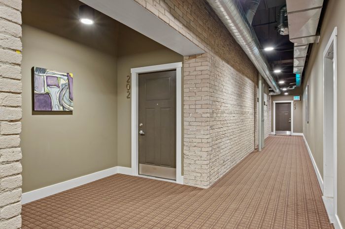 Chic apartment hallway with exposed brick walls and modern lighting, showcasing an inviting entrance to unit 202.