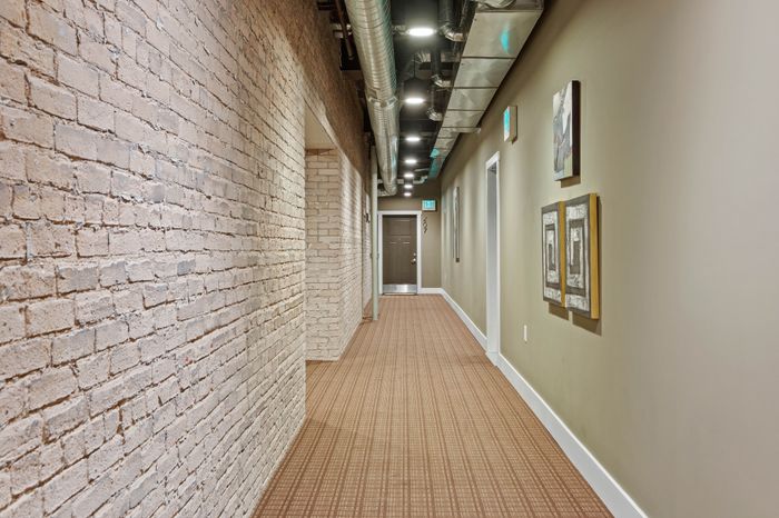 Chic apartment hallway with exposed brick wall, modern lighting, and trendy artwork, leading to apartment door 207.