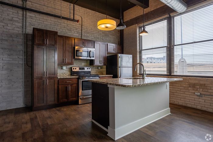 Chic industrial-style kitchen featuring dark wood cabinetry, sleek granite countertops, and modern stainless steel appliances beneath warm pendant lighting.