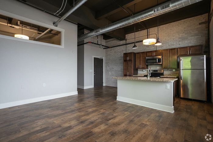 Modern industrial-style apartment showcasing an open-concept kitchen with stainless steel appliances, wooden cabinetry, and exposed ductwork, complemented by chic brick accent walls and warm hardwood floors.