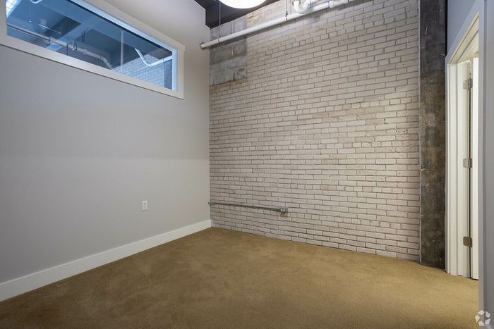 Charming room with exposed brick wall, large window, and cozy carpet flooring.