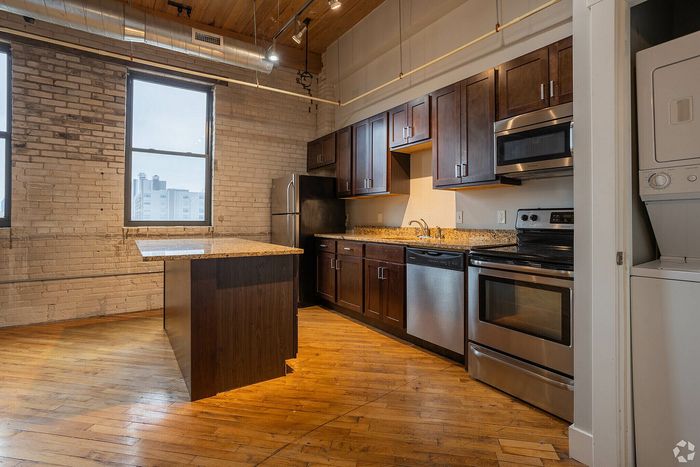 Bright and modern kitchen with stainless steel appliances, granite countertops, and charming exposed brick walls, perfect for urban living.