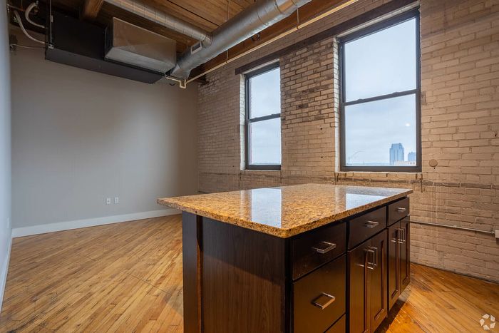 Chic industrial-style apartment kitchen with exposed brick walls, wooden floors, and a modern granite countertop island.