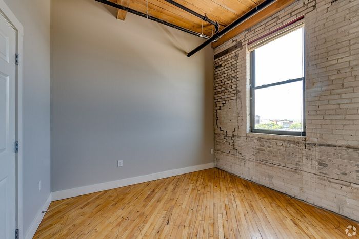 Chic urban loft with exposed brick walls, large window, and warm wooden floors, offering a bright and inviting space.