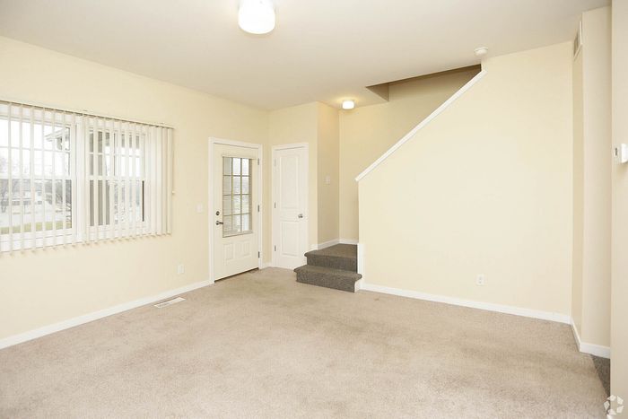 Inviting living area with plush carpeting, natural light from large windows, and modern stairway access.