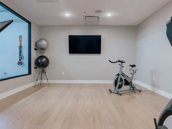 Modern home gym with wooden flooring, exercise bike, gym balls, and large wall-mounted TV.