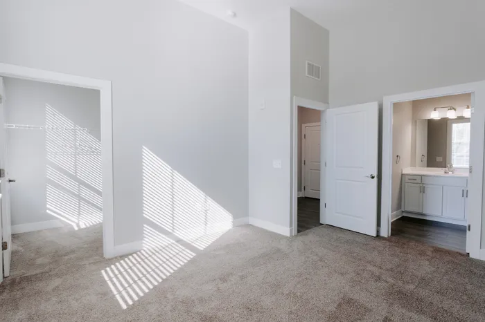 Spacious bedroom featuring soft carpet flooring, built-in closet, and en-suite bathroom with natural lighting.
