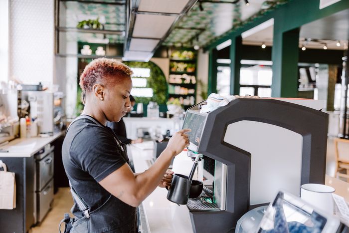 Barista skillfully operating a modern espresso machine in a trendy cafe with lush green decor.