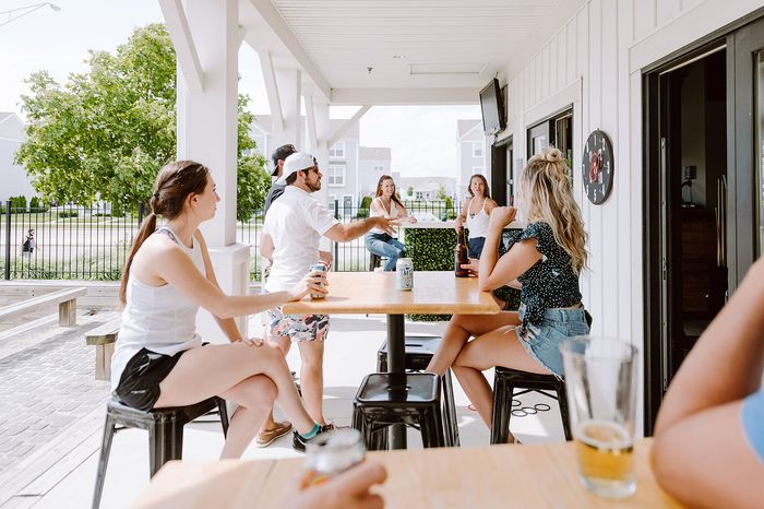 Vibrant outdoor patio gathering with friends enjoying drinks, surrounded by greenery and sunshine.