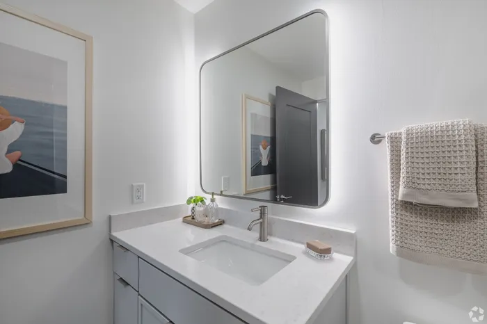 Modern bathroom featuring sleek mirror with ambient lighting, elegant white countertop, and stylish decor.