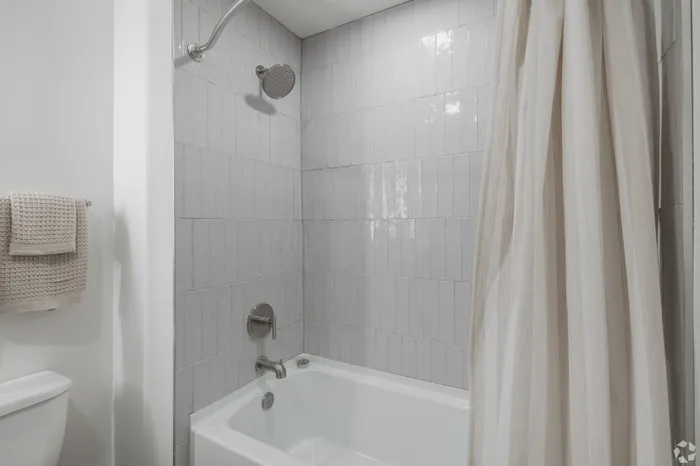 Elegant bathroom showcasing a modern tub with sleek tile walls and a plush towel, creating a serene spa-like atmosphere.