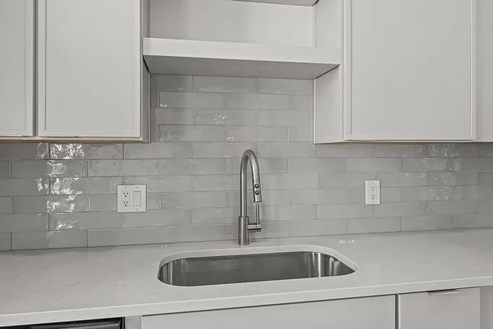 Modern kitchen with sleek gray subway tile backsplash, elegant white cabinetry, and a stylish stainless steel faucet.