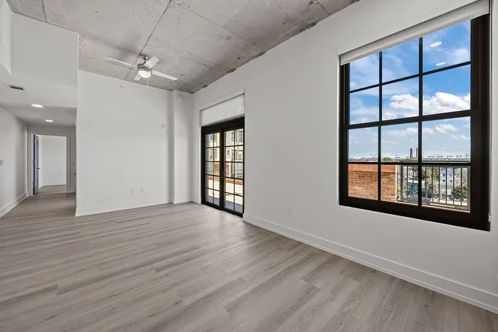 Bright and airy living space featuring modern wooden floors, large windows with a scenic view, and stylish ceiling fan.