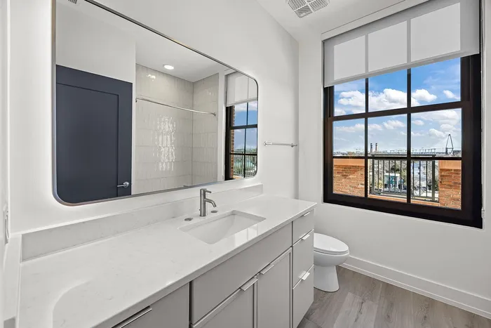 Bright and modern bathroom with a sleek marble countertop, large mirror, and stunning city view from the window.