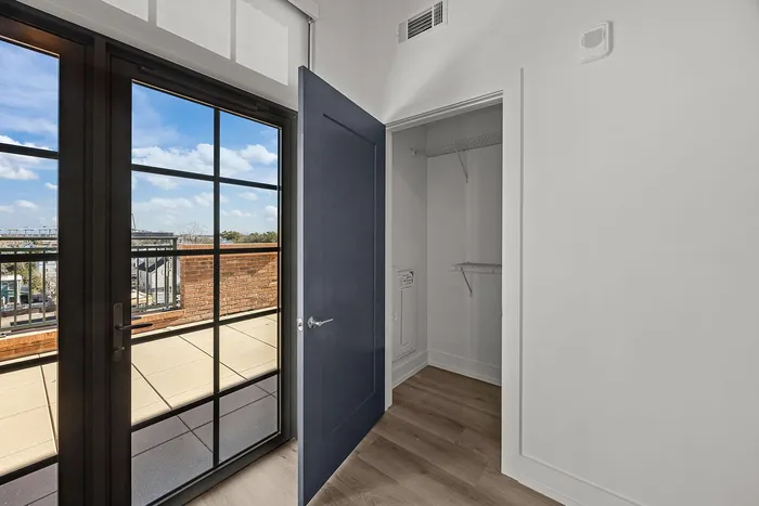 Charming apartment view with large French doors opening onto a sunlit balcony, showcasing stunning sky and cityscape.