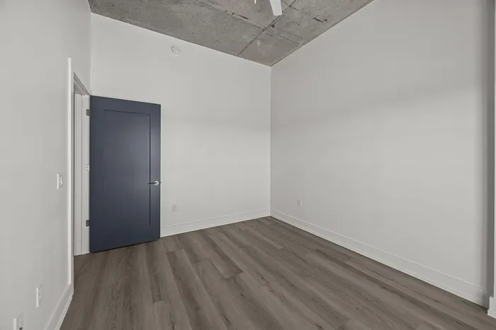 Modern apartment interior featuring sleek wooden flooring, an elegant blue door, and clean white walls with a contemporary concrete ceiling.