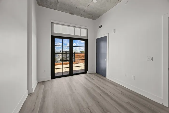 Bright and modern apartment room with large windows, sleek hardwood floors, and an inviting balcony view.