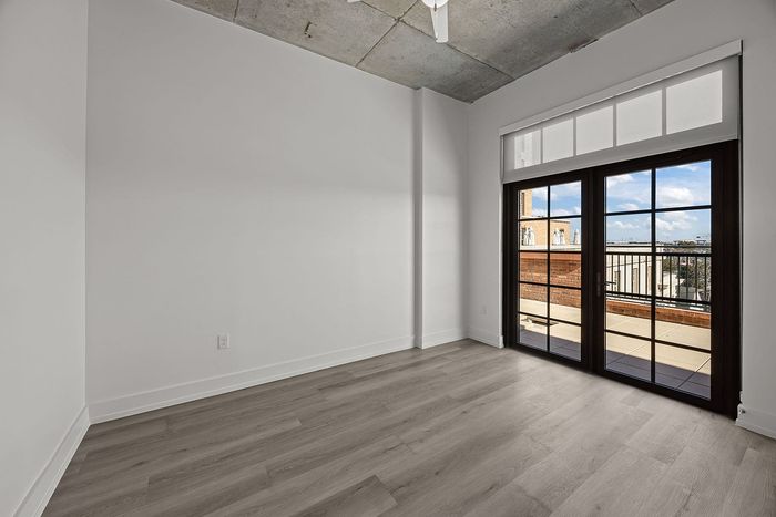 Bright and airy room with floor-to-ceiling windows and sleek wood flooring, opening to a balcony with city views.