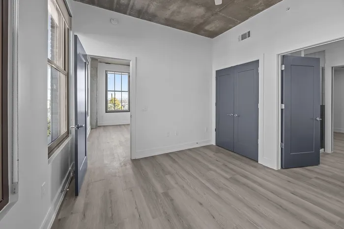 Modern apartment interior featuring light wood flooring, large windows with natural light, and sleek blue doors, offering a refreshing and spacious ambiance.