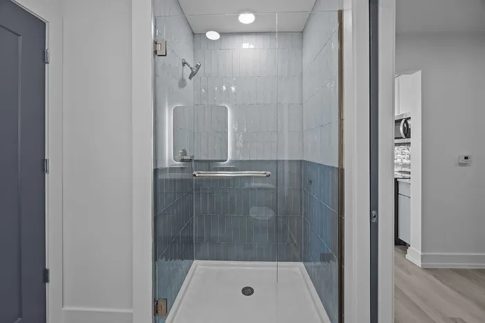 Elegant modern bathroom with sleek glass shower, stylish blue tiles, and ambient lighting.