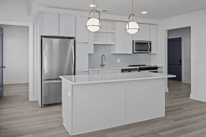 Bright modern kitchen featuring sleek stainless steel appliances, white cabinetry, and an elegant island with pendant lighting.