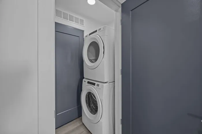 Sleek apartment laundry area featuring a stacked washer and dryer against stylish blue doors, offering modern convenience.