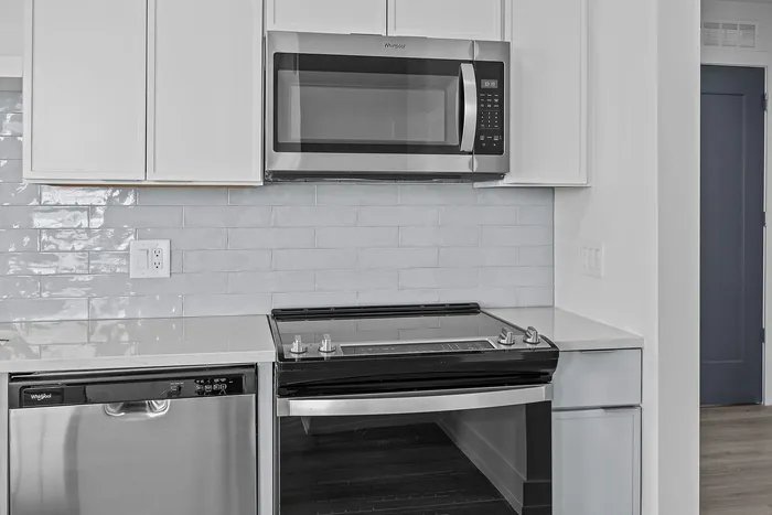 Modern kitchen featuring sleek stainless steel appliances, polished white cabinetry, and a glossy subway tile backsplash.