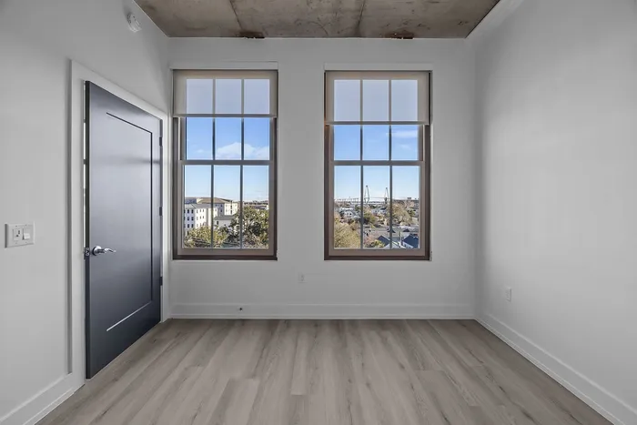 Bright modern room with large windows offering a stunning cityscape view, sleek grey door, and elegant wood flooring.