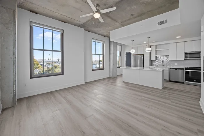 Modern apartment with open-concept design, featuring sleek kitchen with stainless steel appliances, large windows offering scenic views, and chic light fixtures.