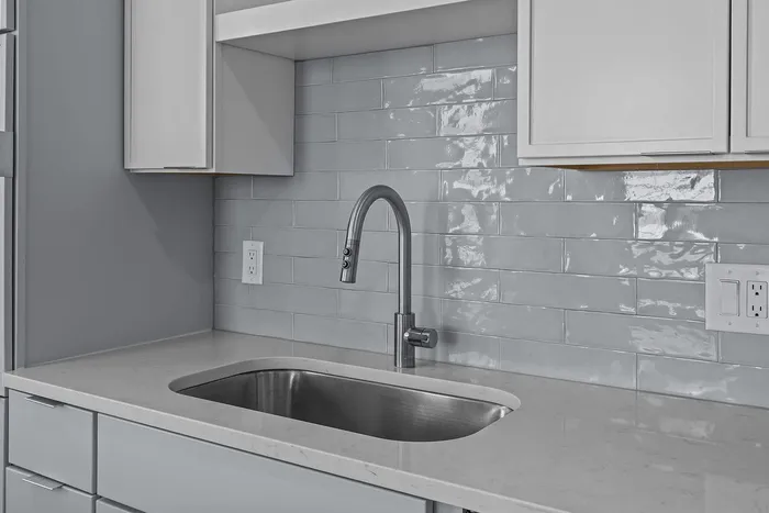 Modern kitchen design featuring a sleek grey tile backsplash, elegant stainless steel faucet, and pristine white cabinetry.