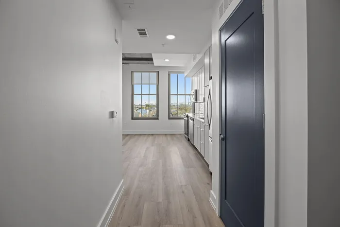 Contemporary apartment hallway leading to a bright living area with large windows and modern kitchen finishes.