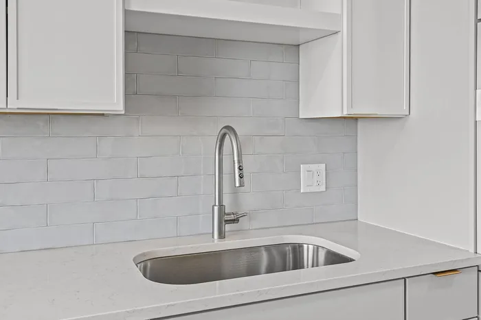 Modern kitchen with sleek marble countertop, elegant stainless steel sink, and stylish white cabinetry.