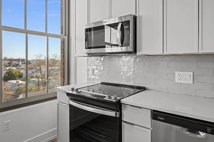 Bright, modern kitchen with sleek white cabinetry, stainless steel appliances, and an expansive window offering scenic views.