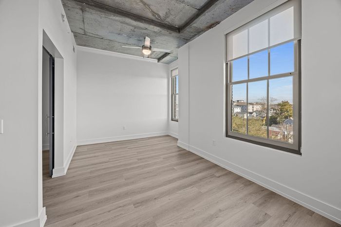 Bright, modern apartment room with large windows, stylish wooden flooring, and an industrial concrete ceiling.