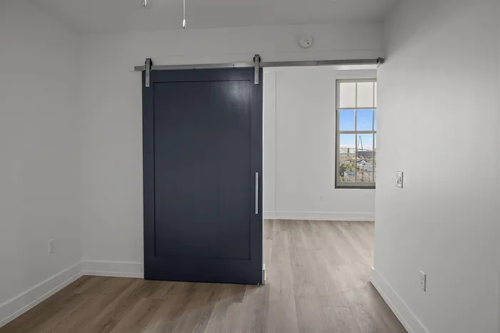 Chic apartment interior featuring a modern navy sliding barn door leading to a bright room with elegant wooden floors and a sunlit window view.