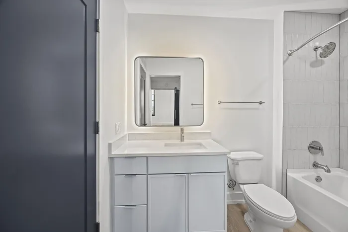 Modern bathroom featuring a sleek vanity with under-cabinet storage, an illuminated mirror, and a pristine bathtub-shower combination.