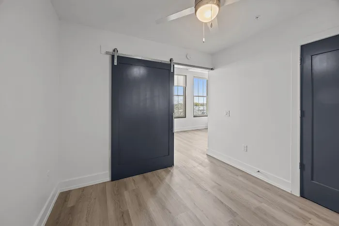 Modern apartment interior with elegant sliding barn door, ceiling fan, and large bright windows showcasing scenic views.