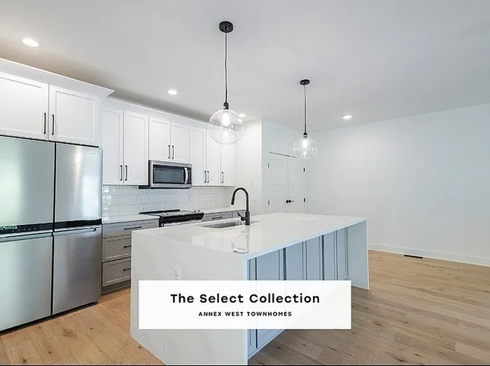 Modern kitchen in Annex West Townhomes with sleek stainless steel appliances, elegant pendant lighting, and spacious white cabinetry.