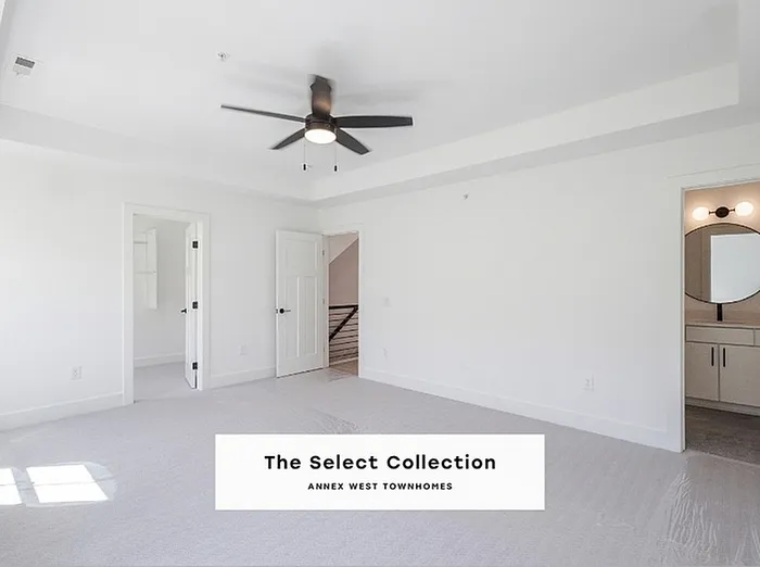 Bright and spacious bedroom in The Select Collection, featuring modern ceiling fan, pristine white walls, and plush carpeting with an adjacent sleek bathroom, perfect for luxurious living.