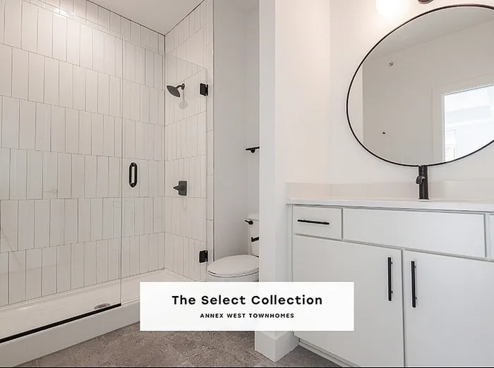 Elegant bathroom in The Select Collection at Annex West Townhomes featuring modern fixtures, sleek glass shower, and stylish round mirror.