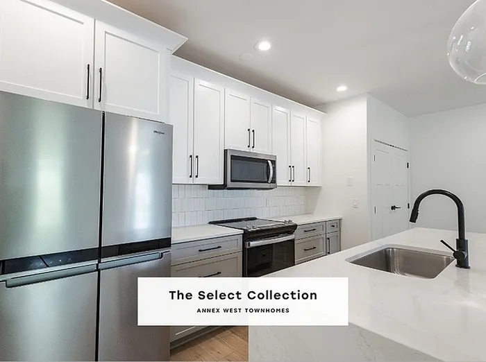 Sleek modern kitchen in Annex West Townhomes with stainless steel appliances, elegant white cabinetry, and a spacious island sink. The Select Collection.