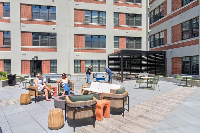 Modern apartment courtyard with stylish outdoor seating, people enjoying leisure activities, and a sleek shaded area.