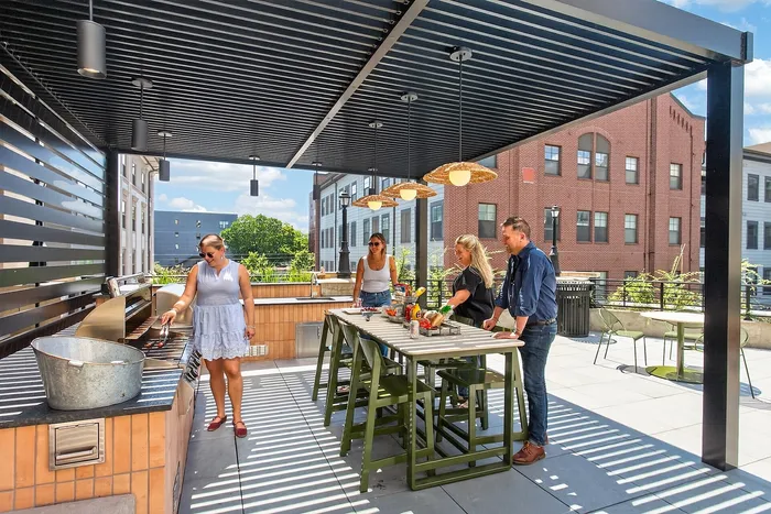 Vibrant rooftop patio with a covered dining area, featuring a group enjoying a modern outdoor kitchen setup.