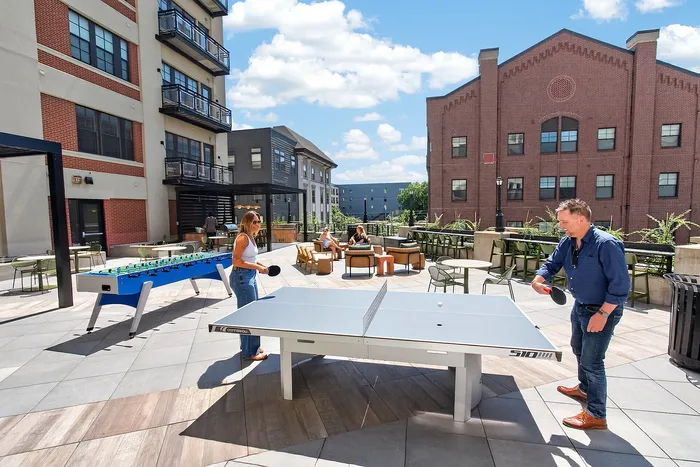 Vibrant outdoor recreation area with a ping pong and foosball table, perfect for social gatherings and leisure in a modern apartment complex.