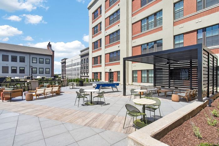 Modern outdoor lounge area with stylish seating, shaded pergola, and vibrant city backdrop.